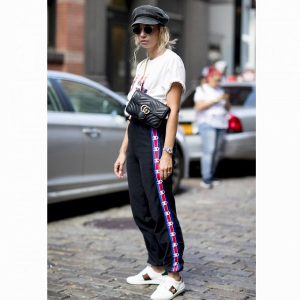 femme blonde portant un jogging champion avec un t-shirt blanc un sac en bandoulière et des baskets