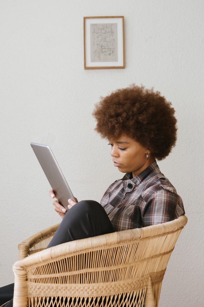 Jeune femme assise dans un fauteuil qui lit sur une tablette